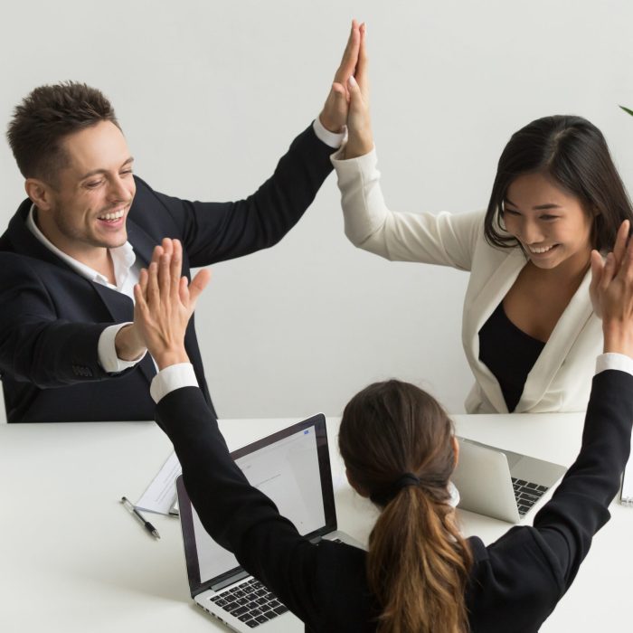 Excited multiracial team giving high five together celebrating victory business success, happy motivated diverse colleagues join palms promising good relations unity, engaging in teambuilding concept